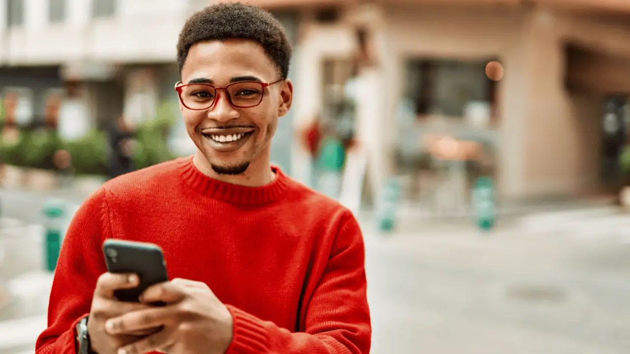 Homem jovem negro sorrindo com celular nas mãos