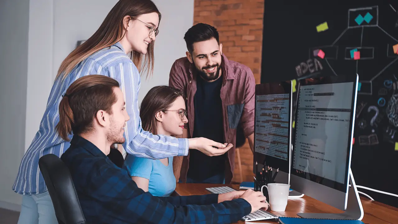 diversas pessoas analisando as telas de dois computadores.